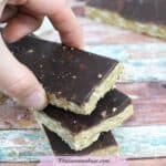 Three homemade protein bars with chocolate on top stacked with a hand placing the last one on top.