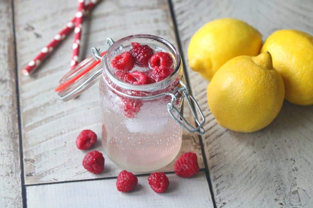 Raspberry lemonade mocktail in a mason jar with raspberries, lemons and straws around it