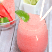 Pink watermelon slushie in a glass garnished with lime and more watermelon and lime behind it