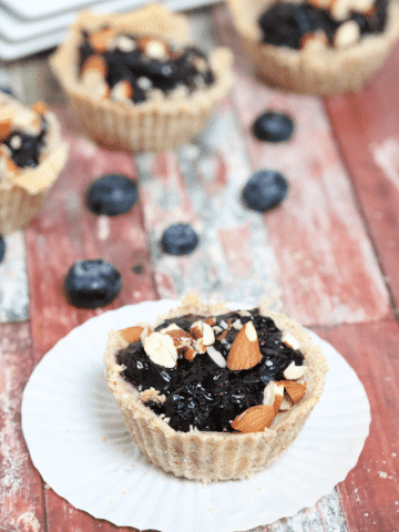 Blueberry tart with almond flour crust on a white muffin tin with blueberries and more tarts behind it.