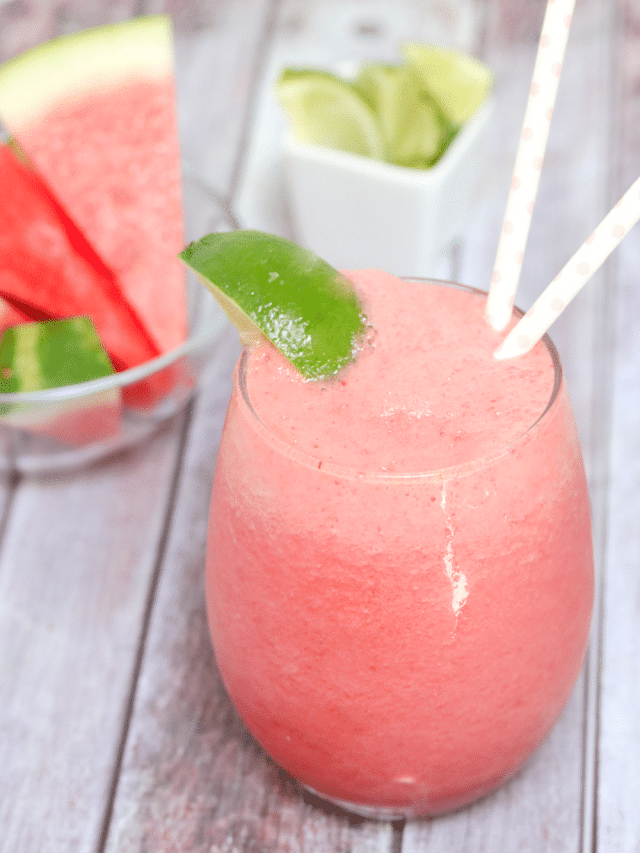 Pink watermelon slushie in a glass garnished with lime and more watermelon and lime behind it