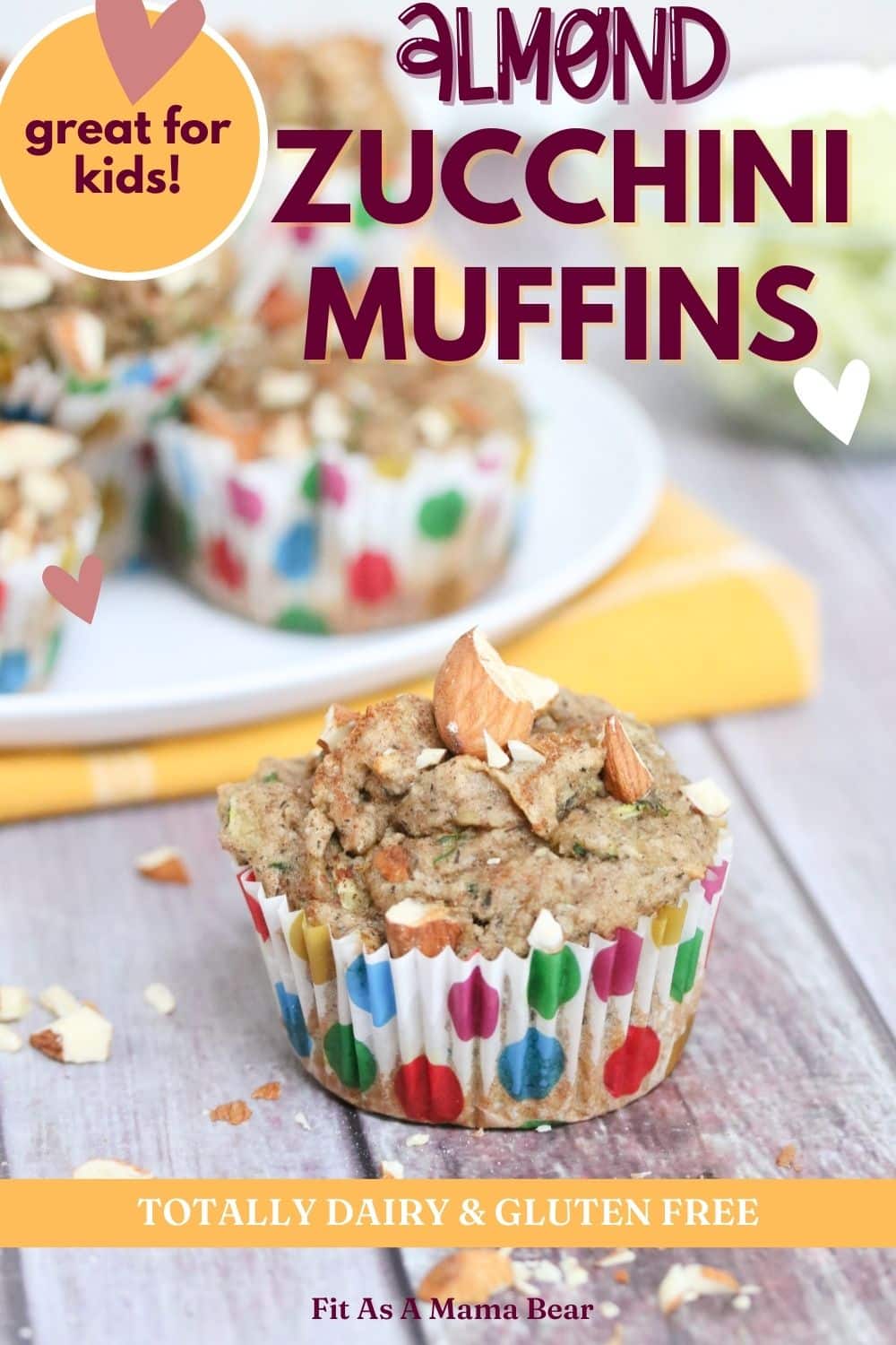 almond zucchini muffin in a polkadot muffin cup in front of more muffins on a white plate and yellow napkin
