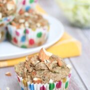 almond zucchini muffin in a polkadot muffin cup in front of more muffins on a white plate and yellow napkin