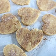 Coconut flour sugar cookies in heart shapes on parchment paper sprinkled with cinnamon and sugar
