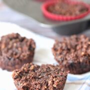 three muffins on a blue linen with more muffins in a muffin tin behind it