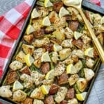 Roasted chicken, potatoes, and asparagus with lemons on a baking tray on a checkered red linen.