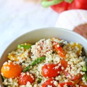 Tan bowl with veggie and quinoa salad in it and bright bell peppers behind it.