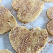 Coconut flour sugar cookies in heart shapes on parchment paper sprinkled with cinnamon and sugar.