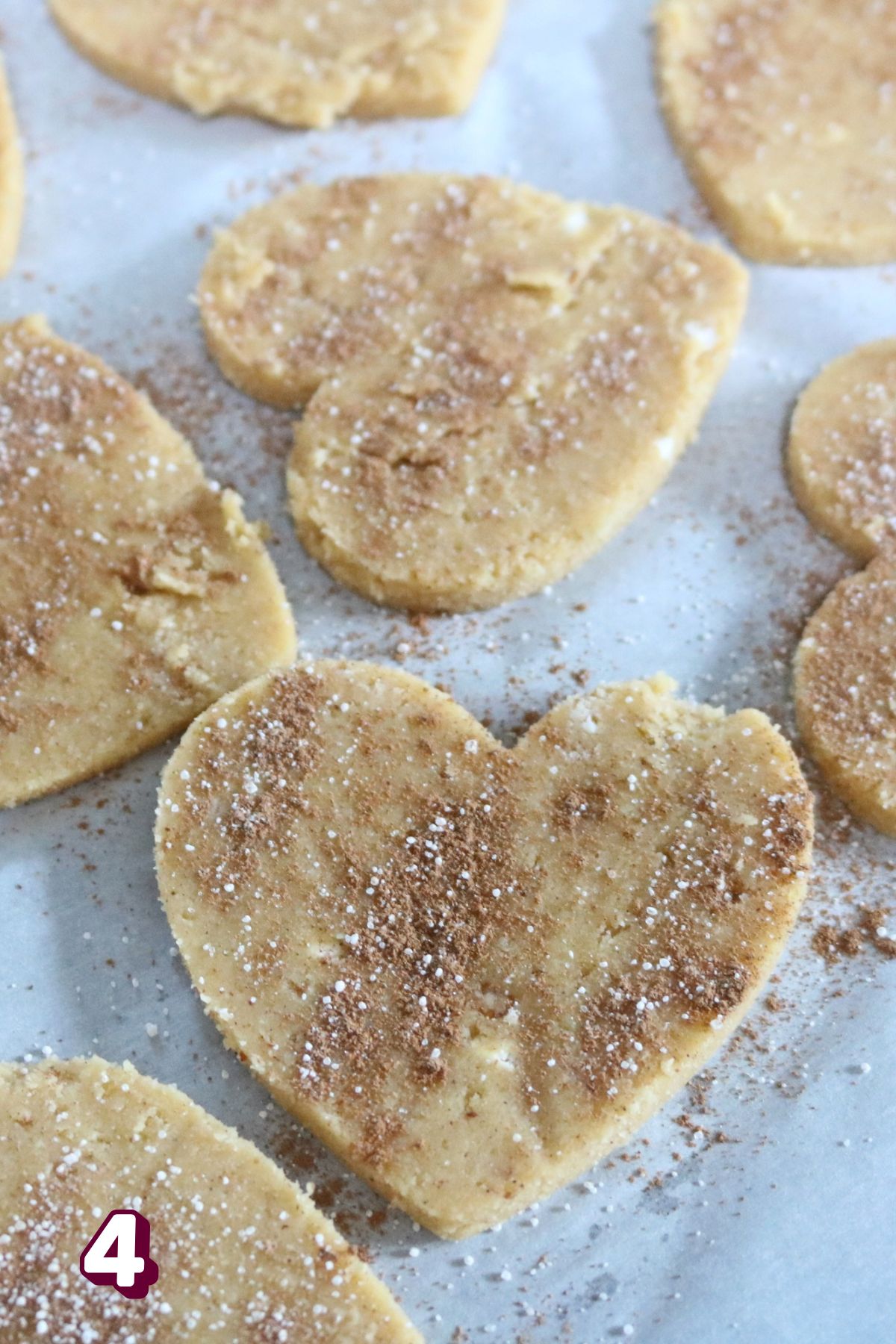Coconut flour sugar cookies in heart shapes on parchment paper sprinkled with cinnamon and sugar.