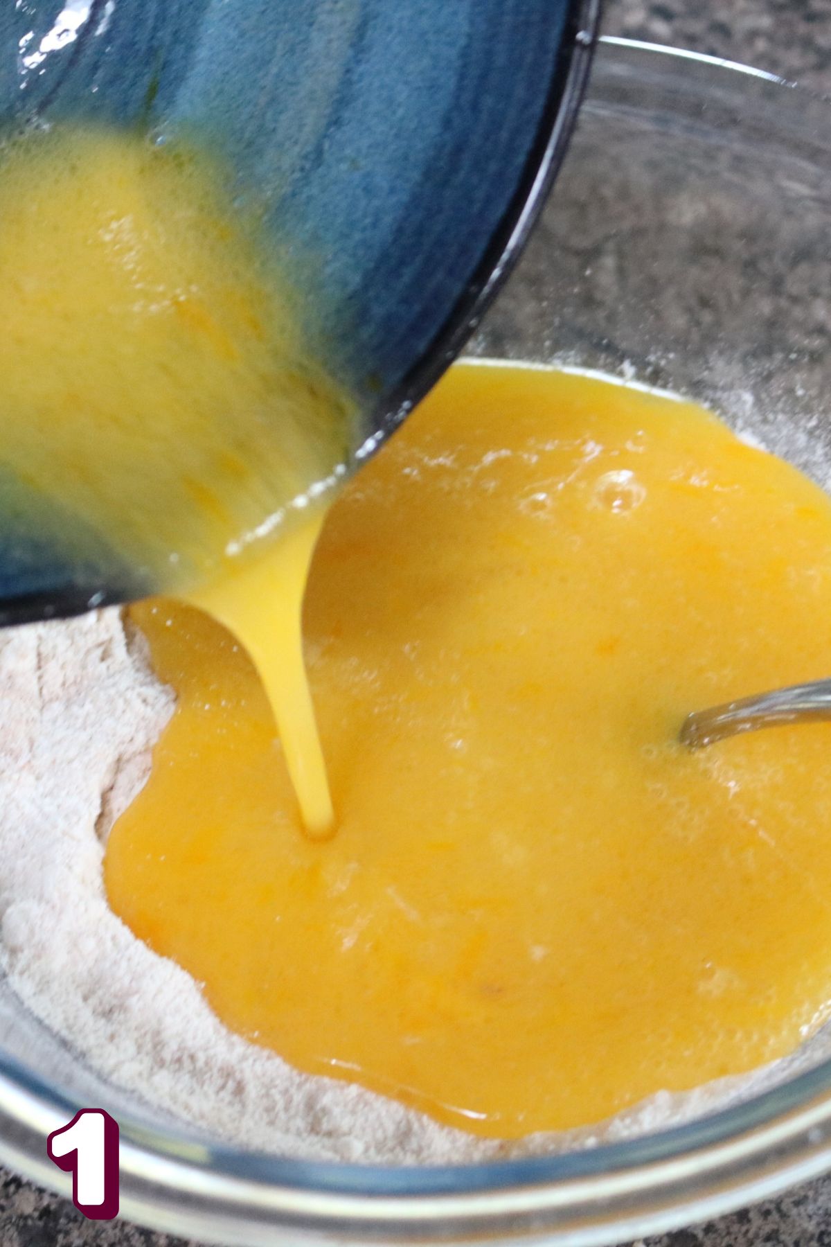 Raw egg being poured from a blue bowl into a glass bowl with flour in it.