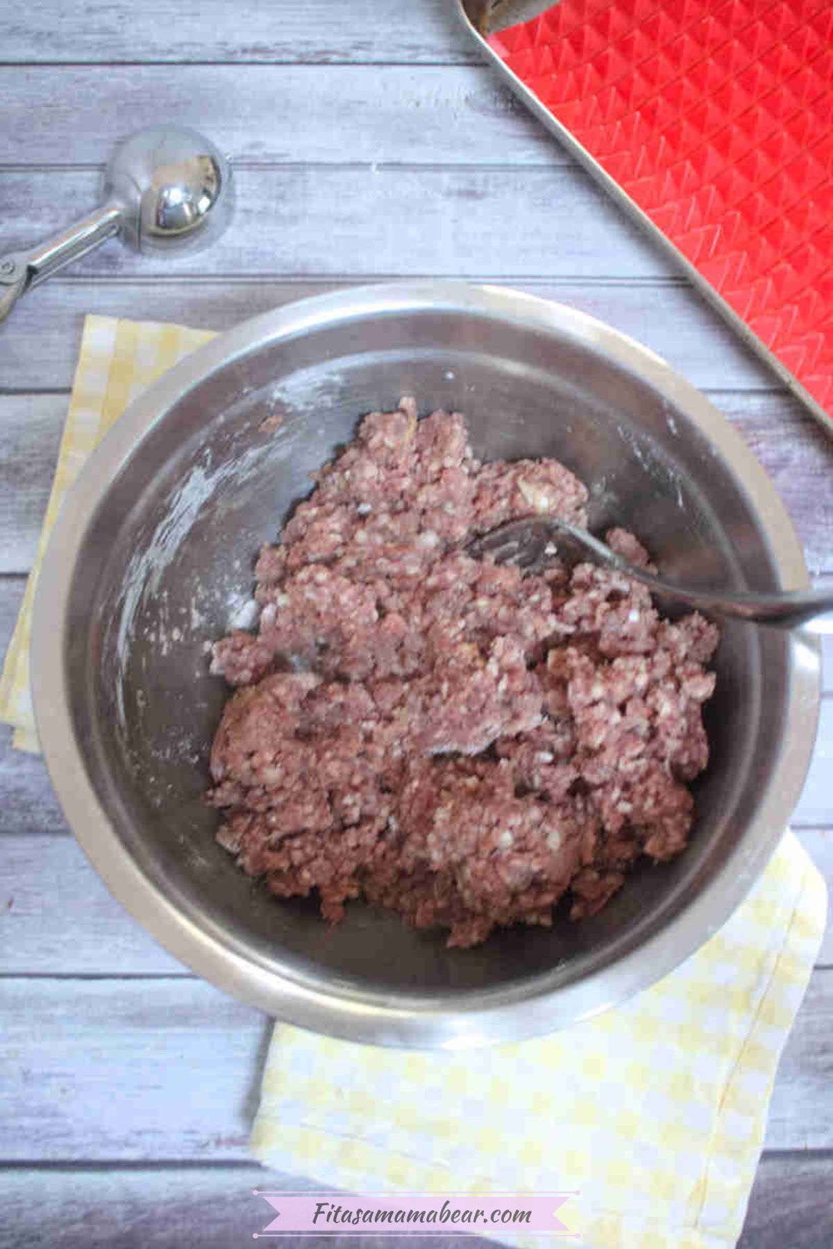 Steel bowl with raw ground beef on a yellow linen with a fork in the bowl.