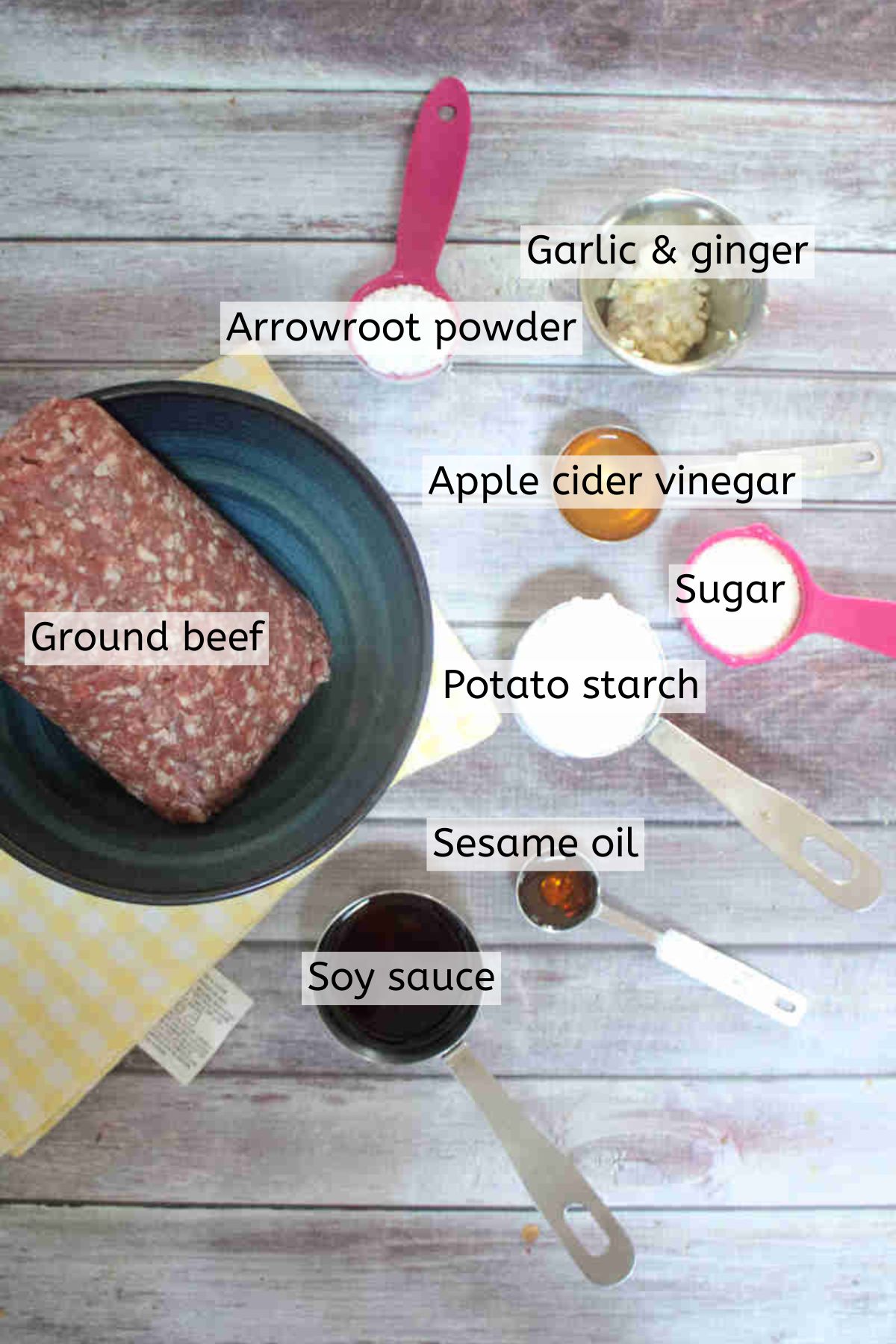 Ingredients to make teriyaki meatballs like ground beef, arrowroot powder and more in measuring cups with text labels over top.