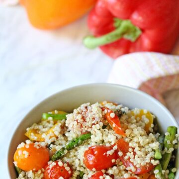 Tan bowl with veggie and quinoa salad in it and bright bell peppers behind it.