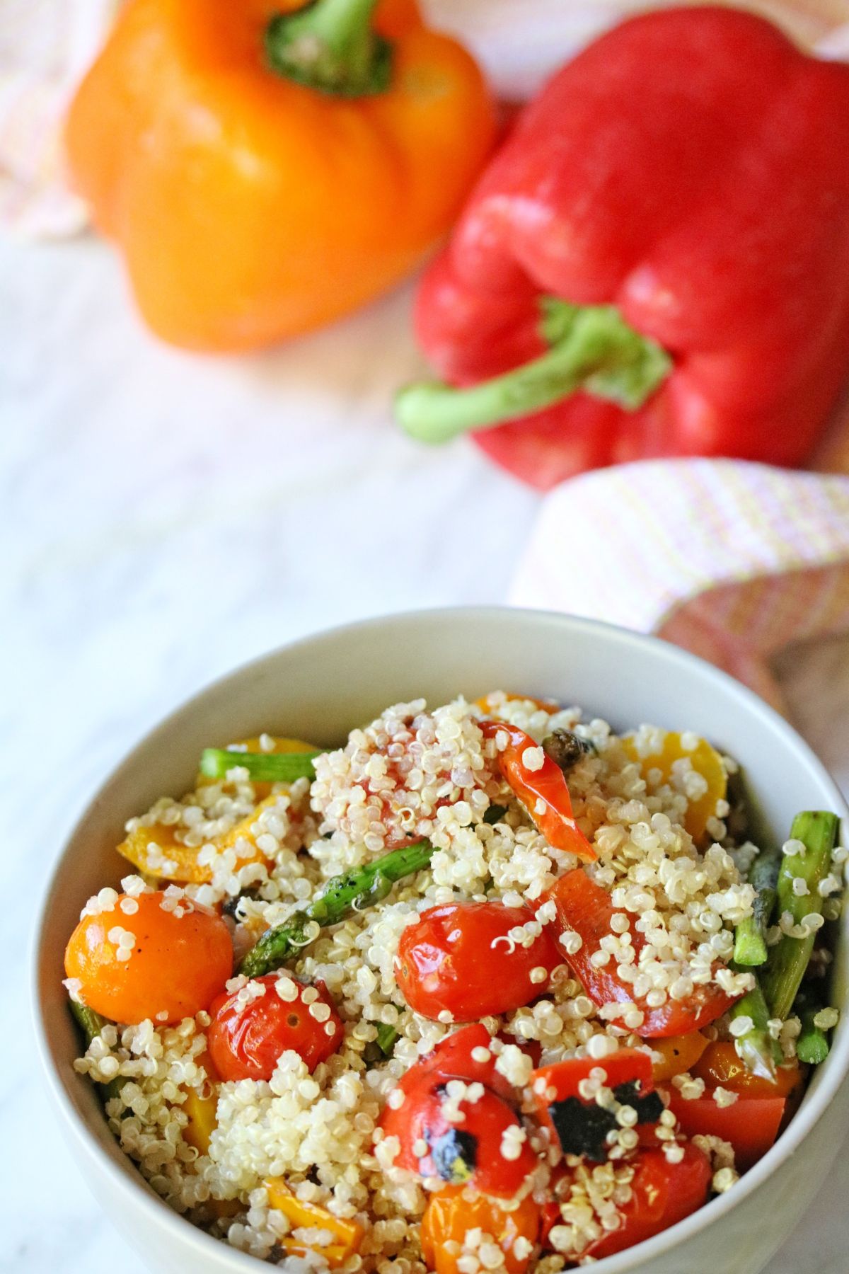 Tan bowl with veggie and quinoa salad in it and bright bell peppers behind it.