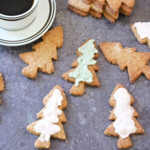 Almond flour sugar cookies in Christmas tree shape dusted with cane sugar and iced in light pink and green around a cut of coffee.