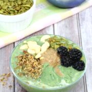 green smoothie bowl with nuts, seeds and berries on top and more topping ingredients behind it in bowls