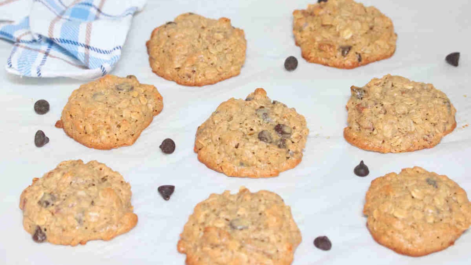 Oatmeal cashew cookies with chocolate chips on parchment paper with chocolate chips around them.