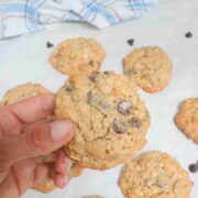 Hand holding up a gluten-free cashew cookie with chocolate chips over more on parchment paper.