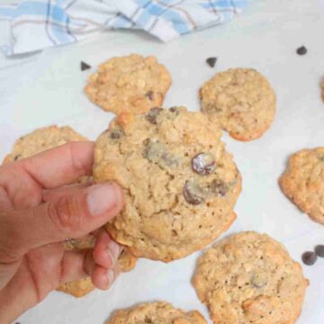 Hand holding up a gluten-free cashew cookie with chocolate chips over more on parchment paper.