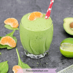 featured image with text: tropical green smoothie with red straws in the glass and orange, spinach, avocado and lime around it