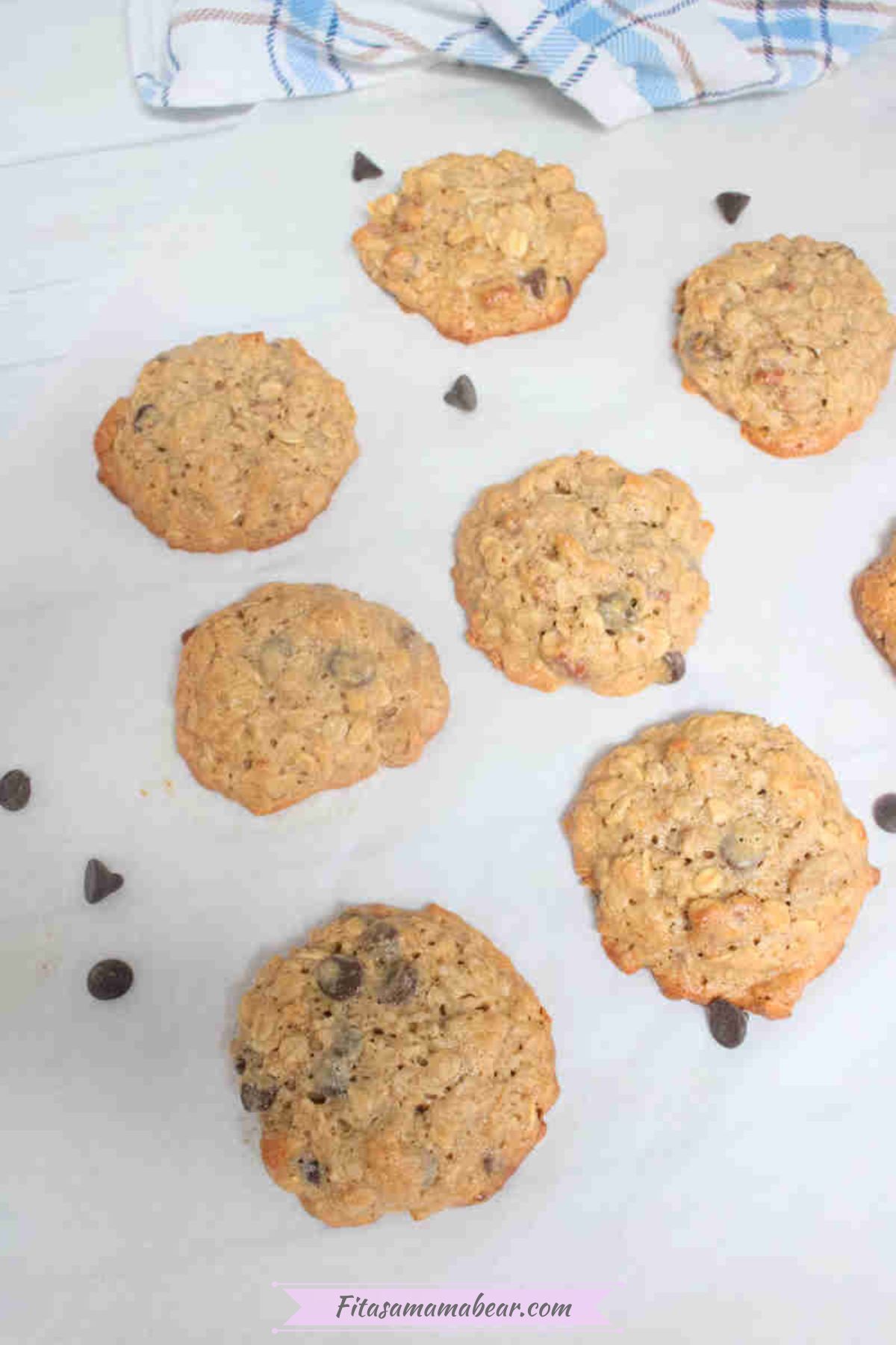 Oatmeal cashew cookies with chocolate chips on parchment paper with chocolate chips around them.