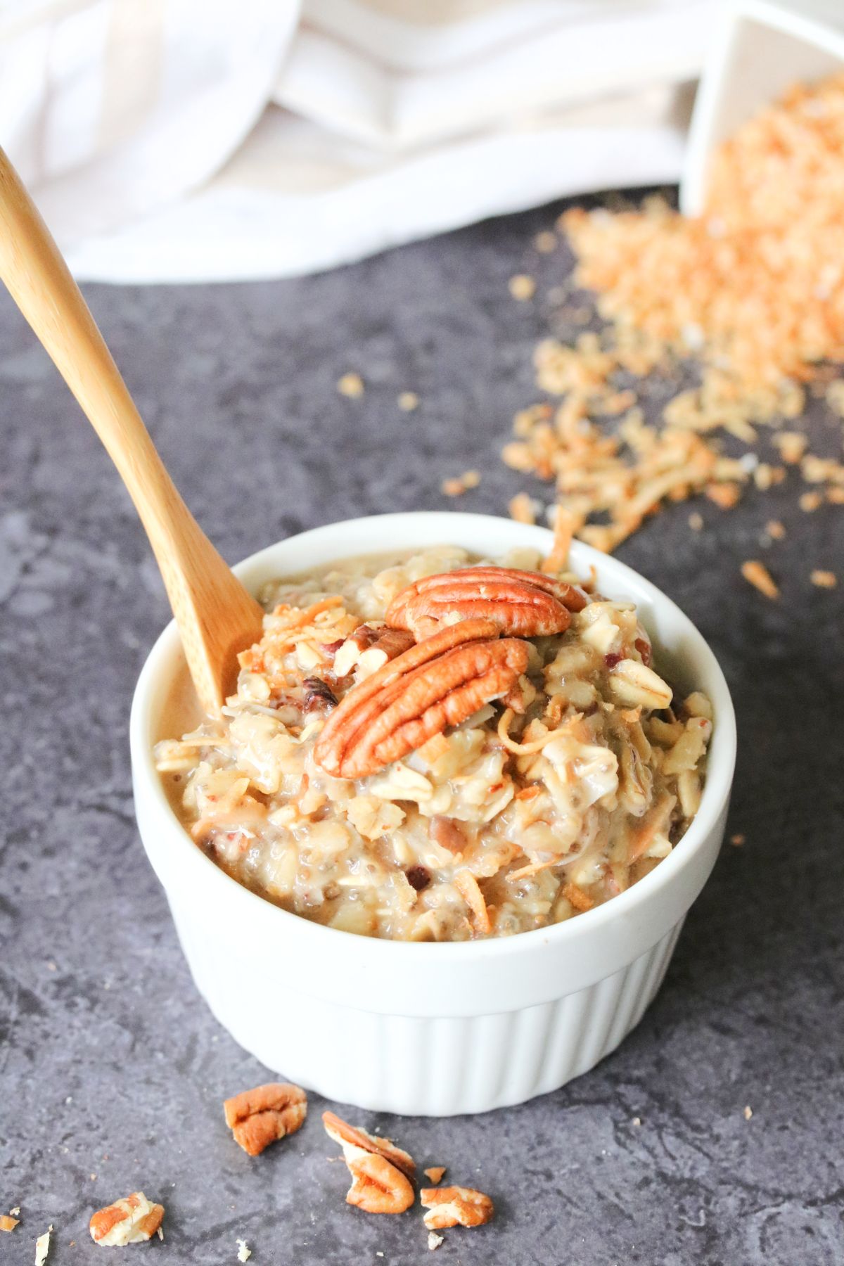 White ramekin with oatmeal topped with pecans and a wooden spoon in the ramekin.