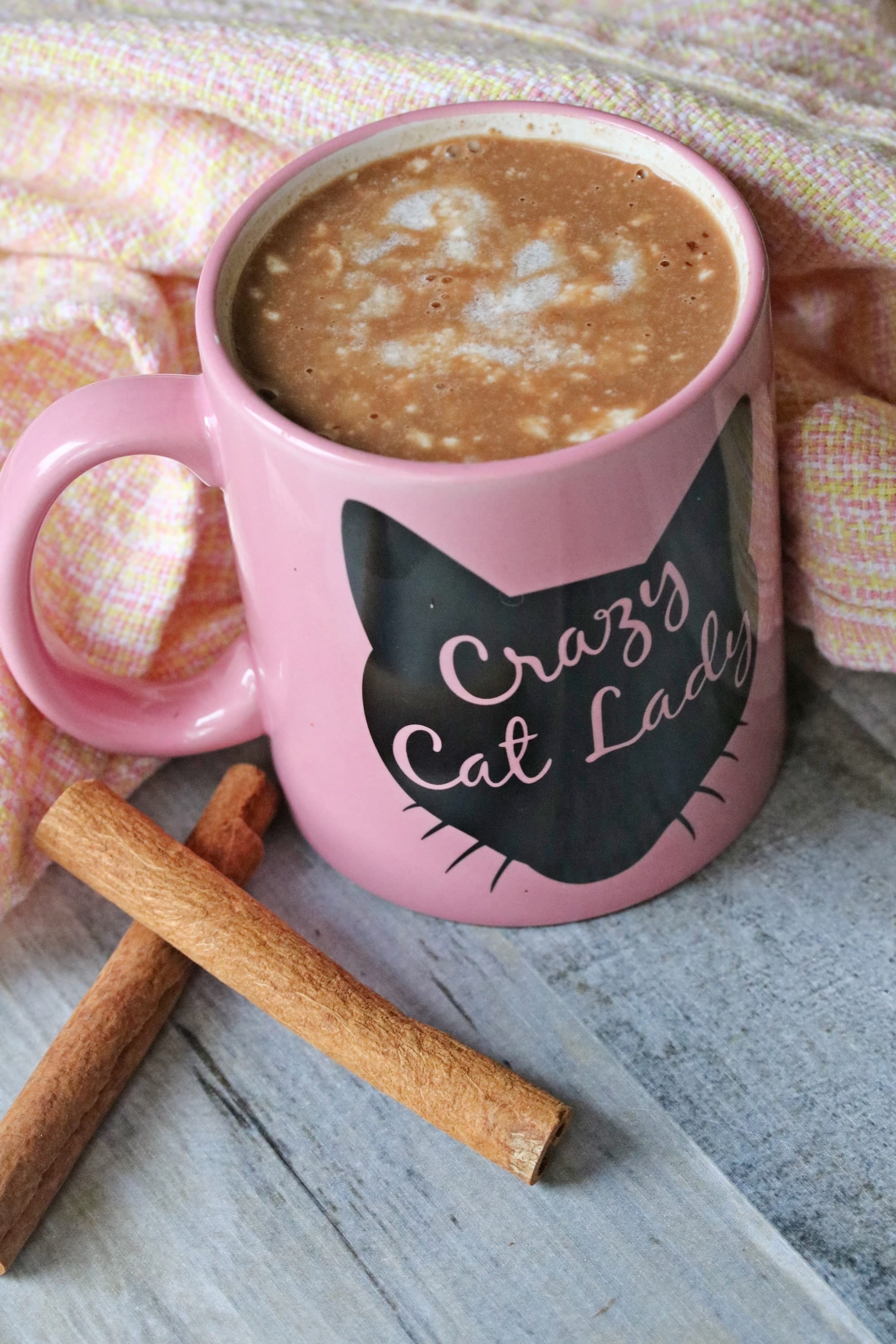 Homemade hot chocolate in pink crazy cat lady mug with cinnamon sticks beside it