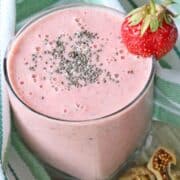 Strawberry smoothie in a glass with chia seeds on top and a strawberry on the glass.
