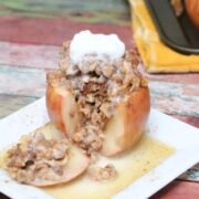 Baked apple stuffed with oatmeal with a slice cut out on a white plate with maple syrup.