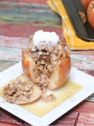 Baked apple stuffed with oatmeal with a slice cut out on a white plate with maple syrup.