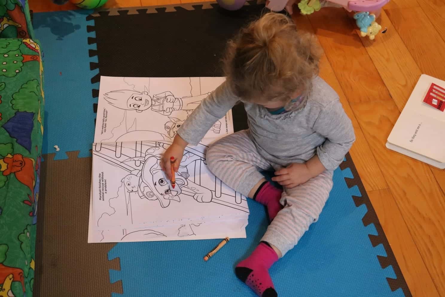 Toddler sitting on the floor with crayons and a paw patrol coloring book
