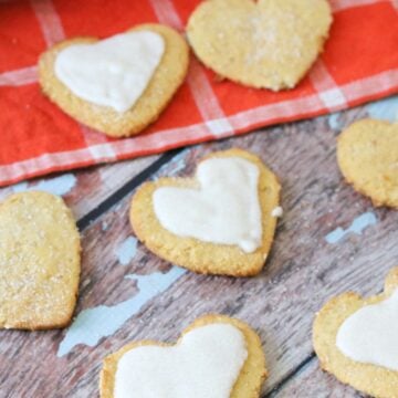Heart shaped coconut flour sugar cookies, some of them iced on an orange linen.