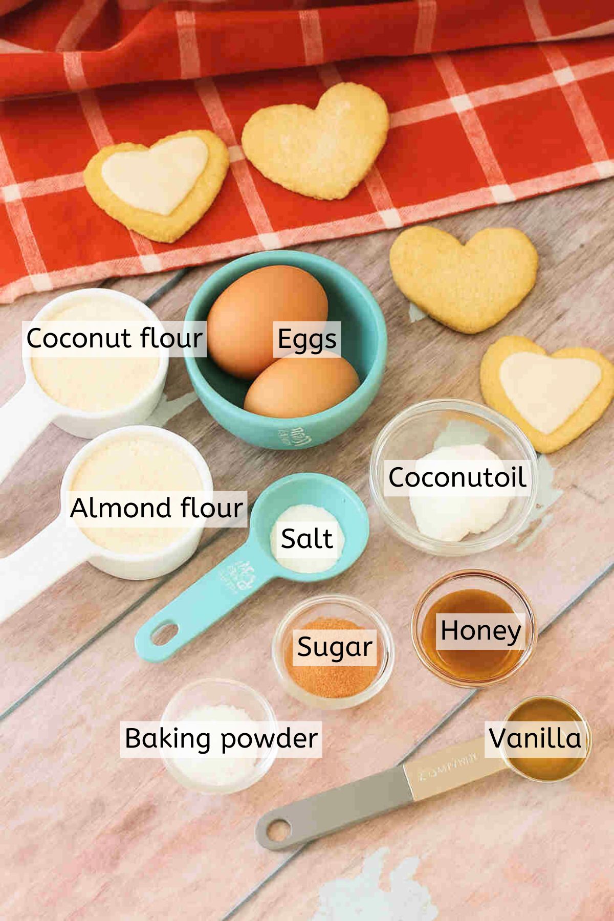 Multiple ingredients like coconut flour, almond flour, and sugar to make sugar cookies in measuring cups with text labels over top.