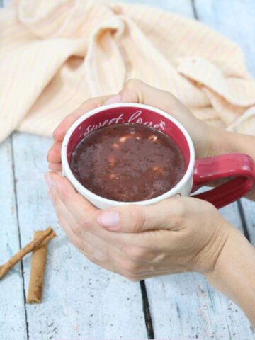 healthy hot chocolate in a white and red mug with hands holding the mug on it and a light linen behind it