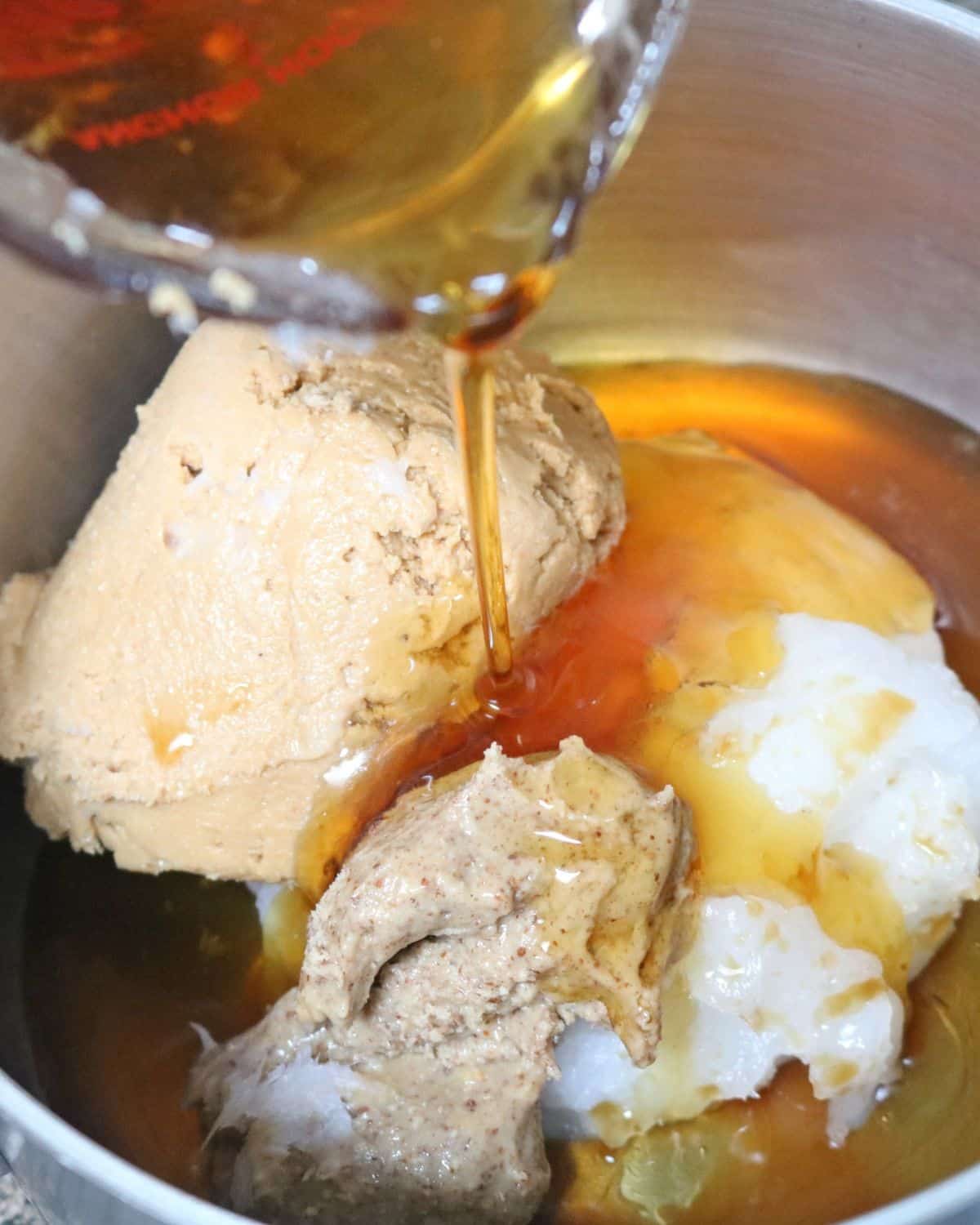 Coconut oil, cashew butter, and maple syrup being poured into a small pot