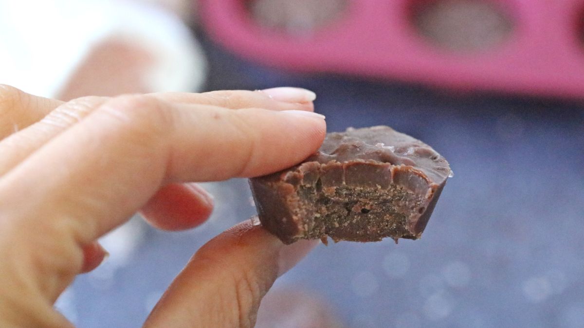 Two fingers holding a piece of keto chocolate fudge up close with a bit out of it.