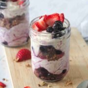 Two mason jars with dairy-free yogurt parfaits layered with yogurt, berries, and granola on a cutting board.