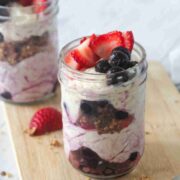 Two mason jars with dairy-free yogurt parfaits layered with yogurt, berries, and granola on a cutting board.