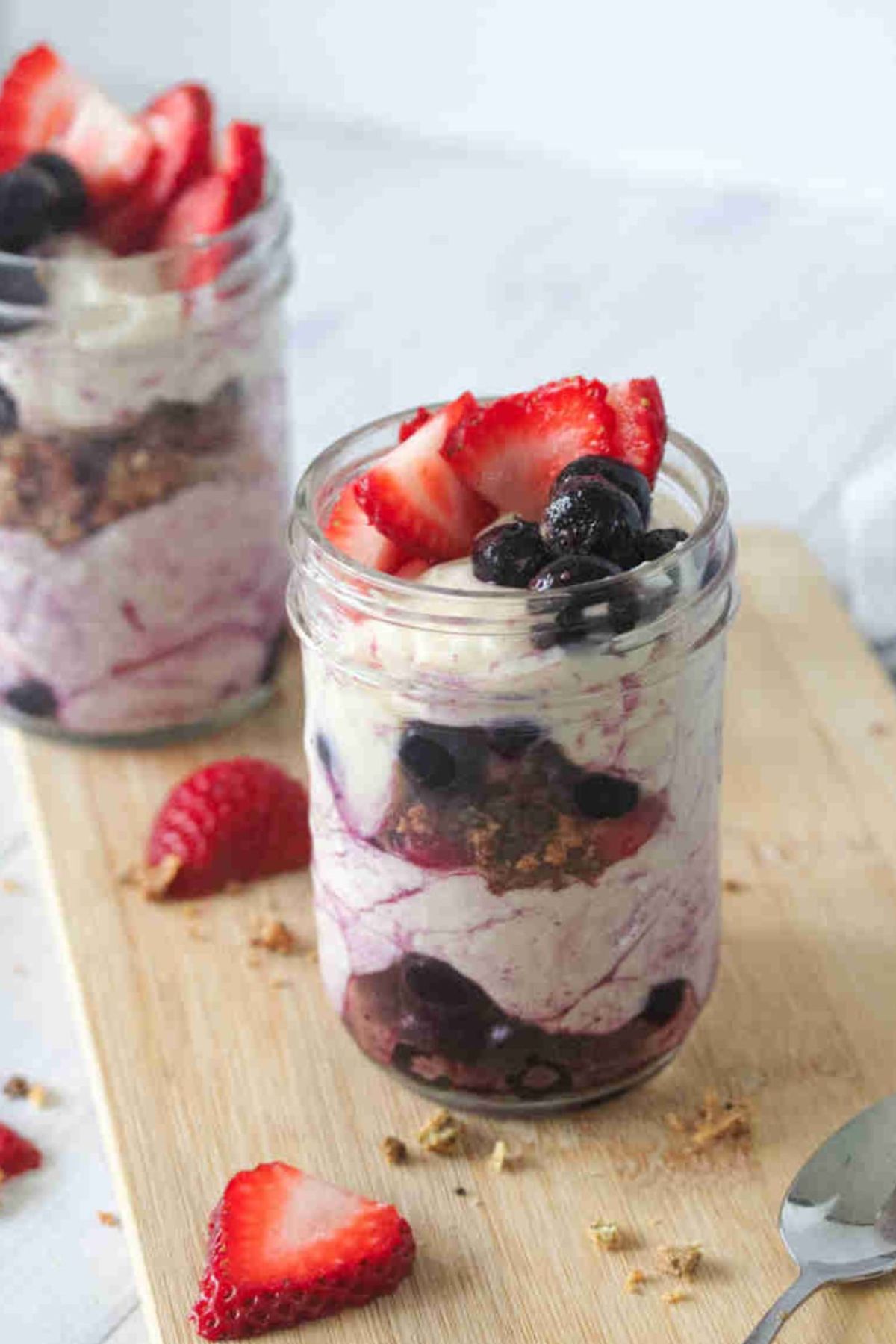 Two mason jars with dairy-free yogurt parfaits layered with yogurt, berries, and granola on a cutting board.