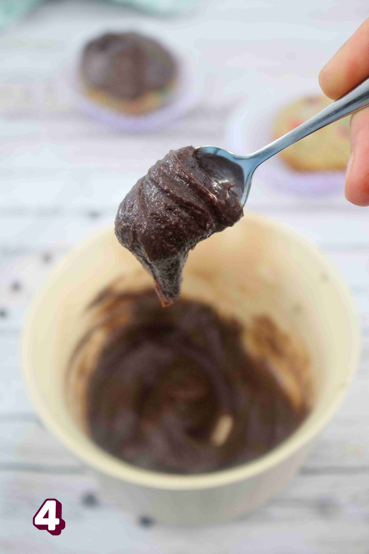 Chocolate frosting on a spoon and more in a tan bowl under it.
