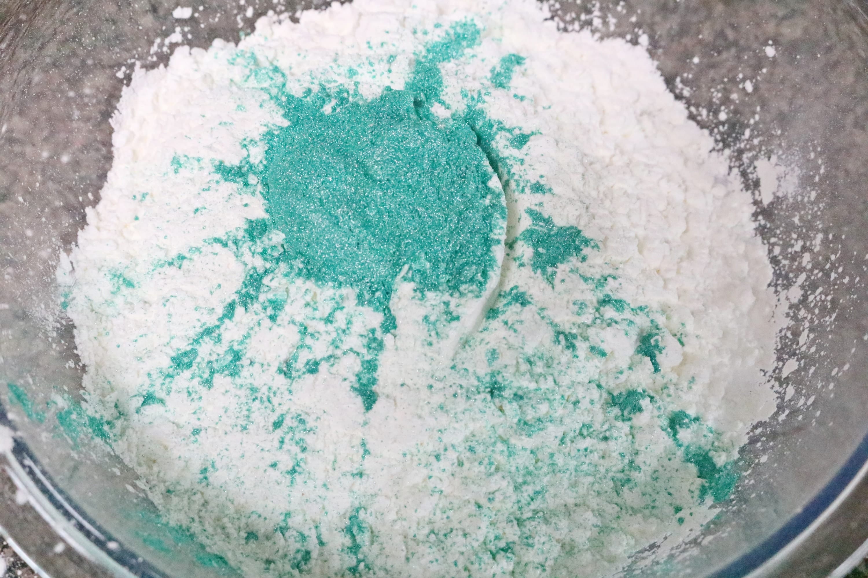 Dry ingredients for homemade bath bombs in a glass bowl with blue mica powder