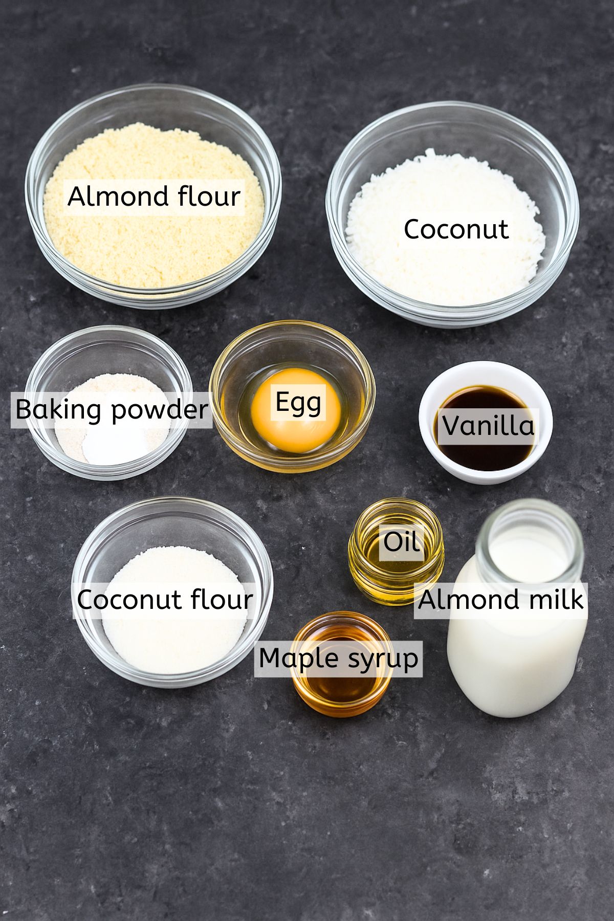 Almond flour, coconut, eggs, oil, and more ingredients in glass dishes with text labels over top.