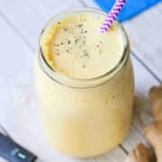 turmeric peach smoothie in a mason jar with a purple straw. Turmeric root and powder and ginger root around it