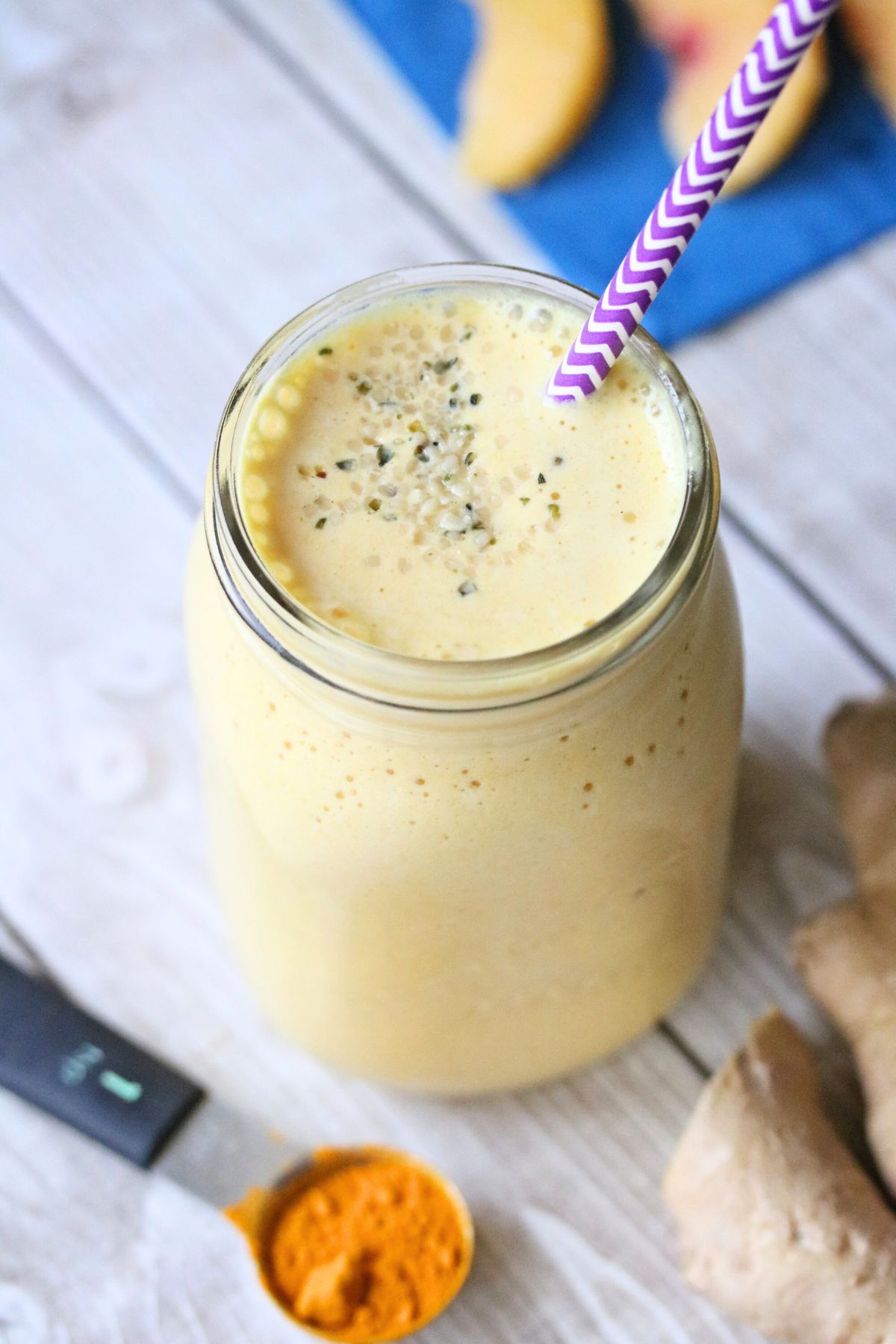 Turmeric peach smoothie in a mason jar with a purple straw. Turmeric root and powder and ginger root around it.
