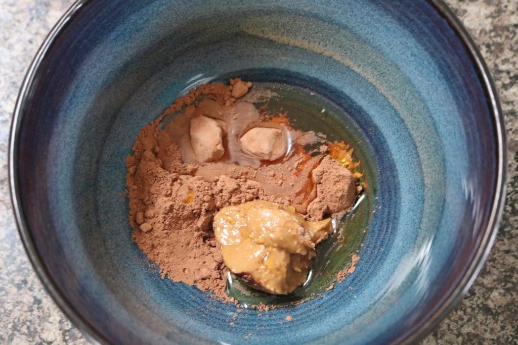 Almond butter, cacao powder, and maple syrup mixed together in a blue bowl