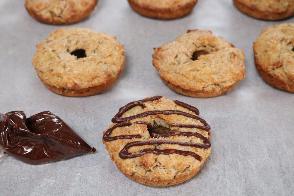 Homemade protein donuts on parchment paper with one donut drizzled with chocolaye