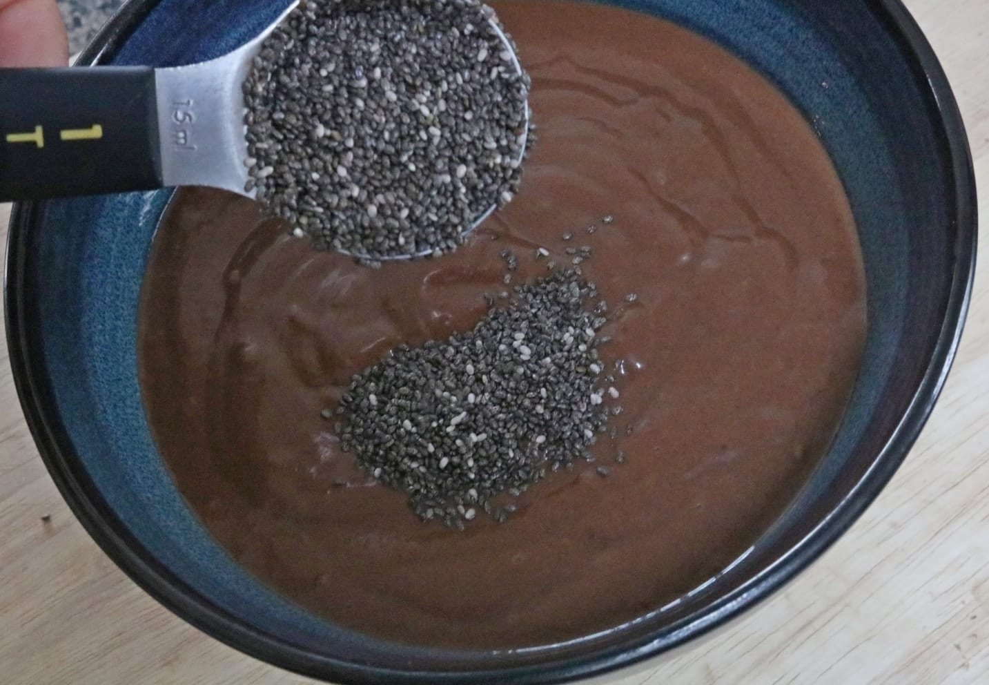 A spoonful of chia seeds being poured over a bowl of chocolate pudding