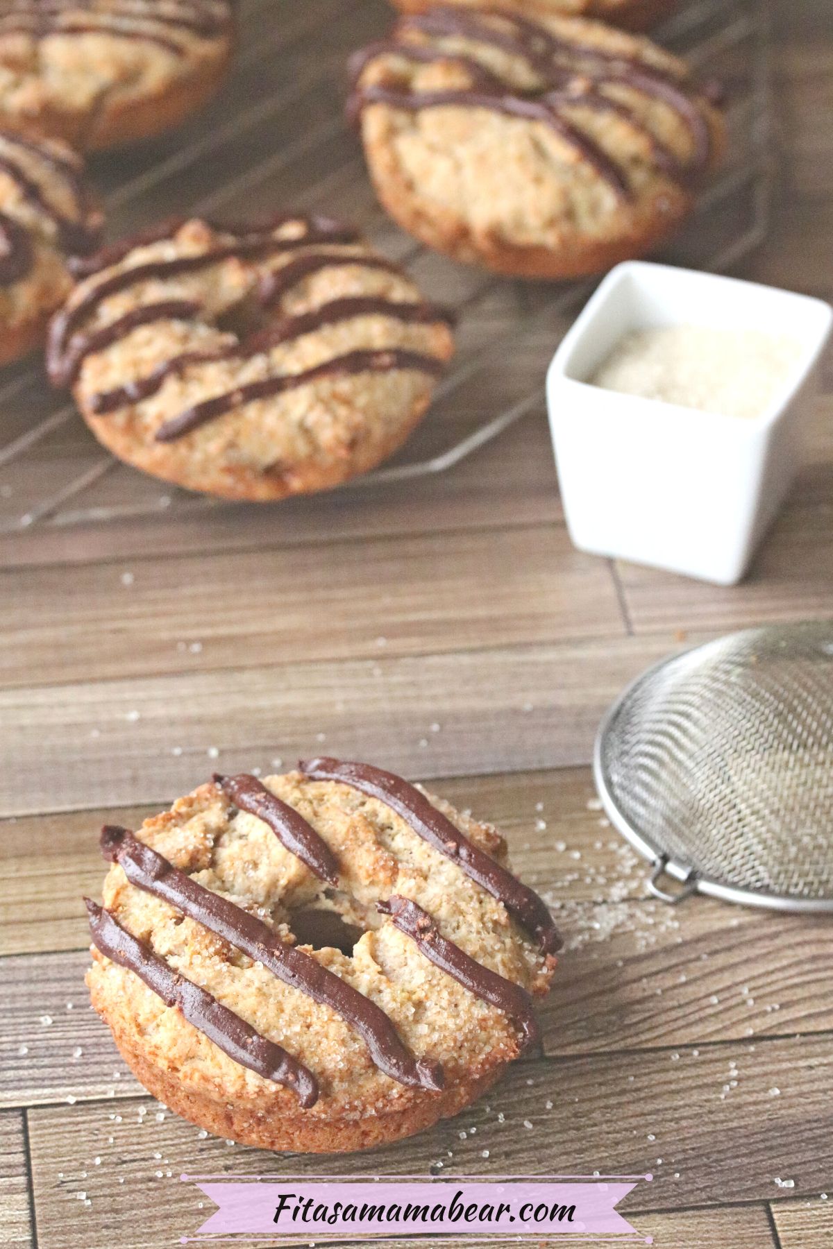 Banana protein donut with chocolate drizzle with more donuts on a cooling rack behind it.