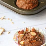 Healthy, sugar free carrot muffin topped with chopped almonds in a colored cupcake liner with more muffins in a muffin tray behind it.