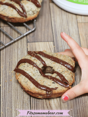 Banana protein donut iced with chocolate sauce with a toddlers hand grabbing it and more donuts on a cooling rack behind them